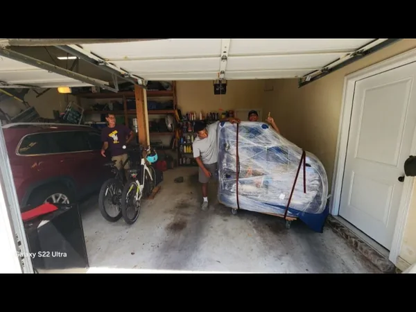 Team members moving a wrapped large furnishing on a wheeled dolly in a garage